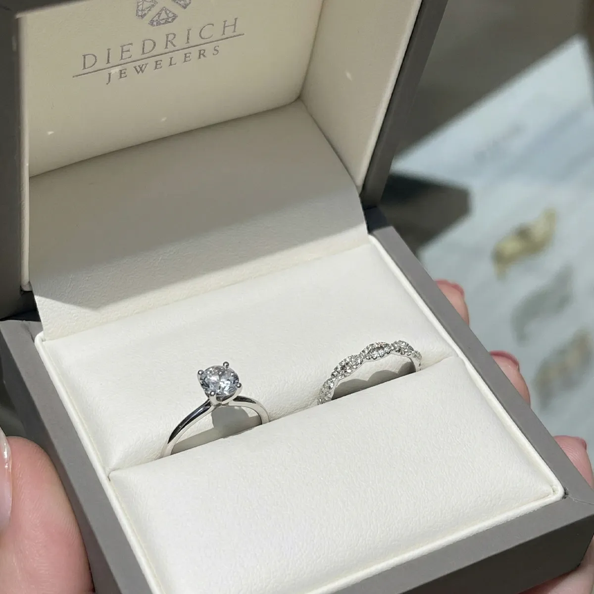 Two rings in a jewelry box from Diedrich Jewelers; one with a solitaire diamond, the other with a diamond band.