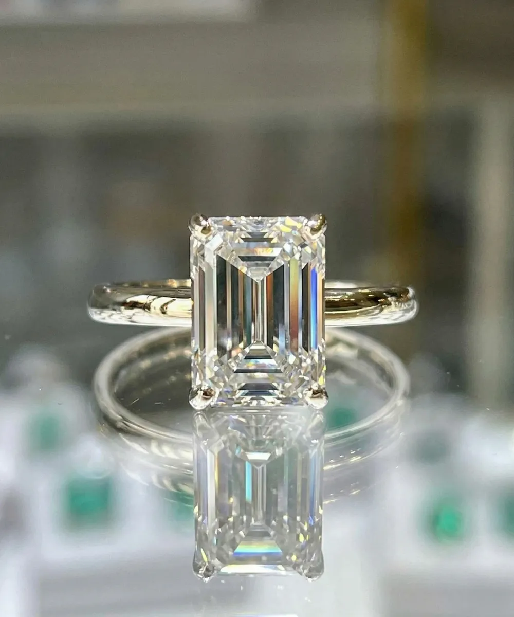 Emerald-cut diamond ring with gold band on reflective surface at Diedrich Jewelers.