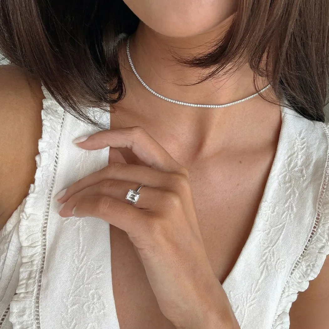 Woman wearing a white dress, diamond ring, and necklace.