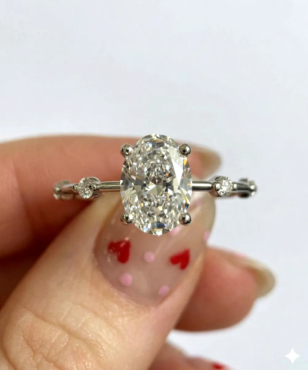 A hand holding an oval diamond ring with a decorative band.