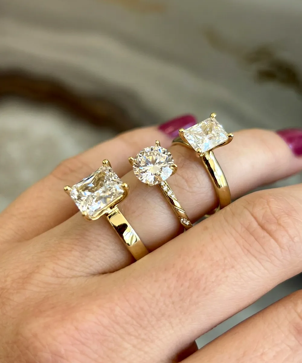 Three gold rings with large diamonds on a person's fingers.