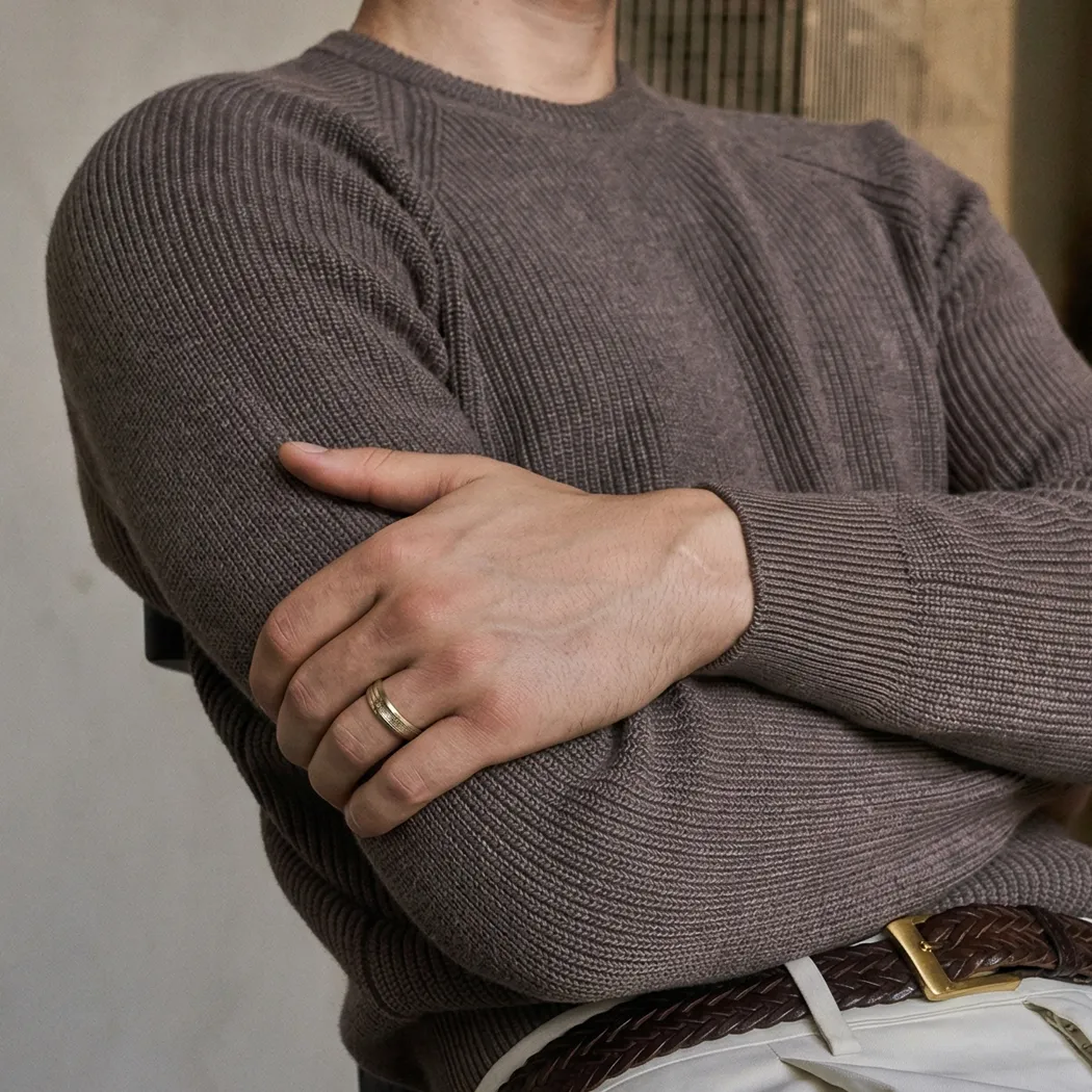 Man wearing a brown sweater with arms crossed, showcasing a gold ring on his finger.