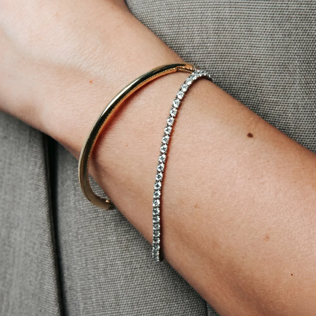 Two elegant bracelets on a wrist: one gold and one diamond-studded.