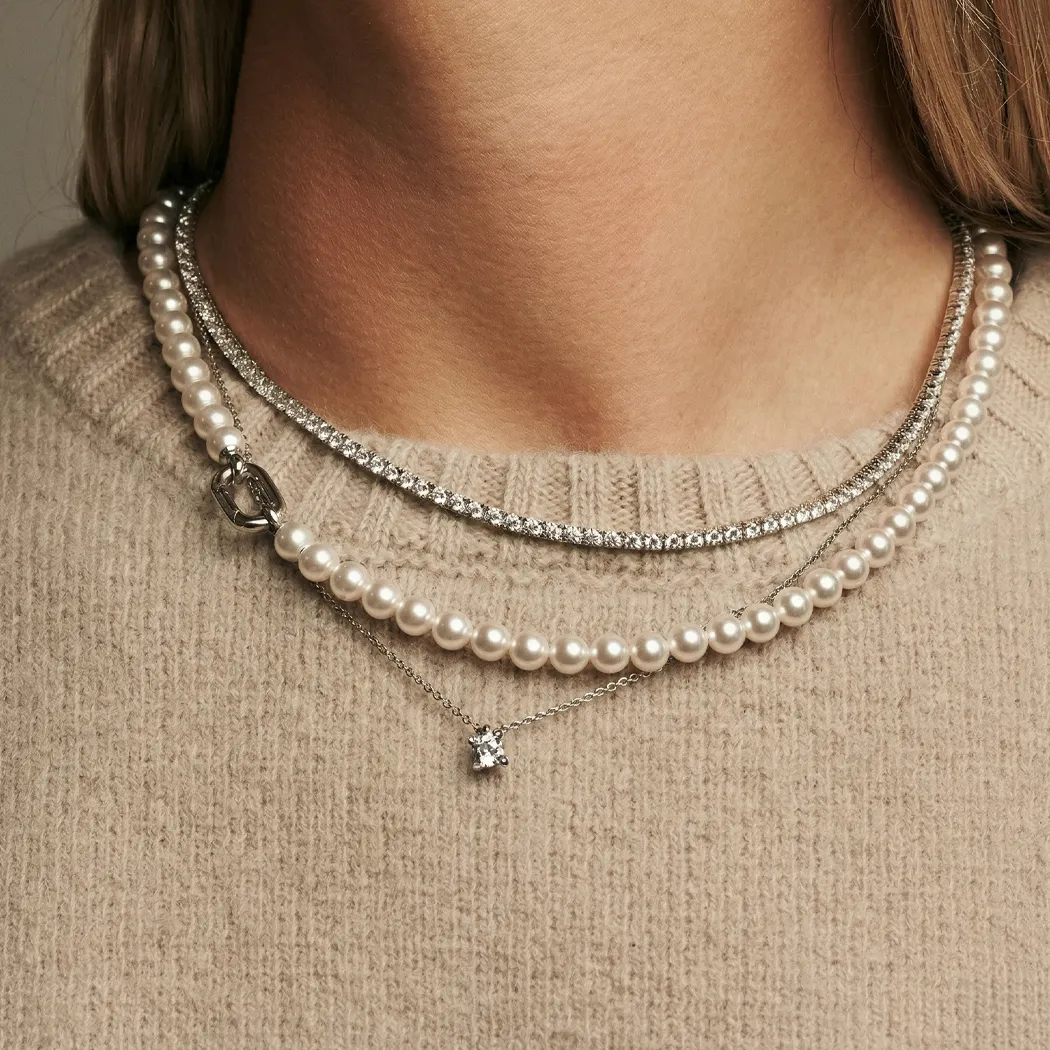 Layered pearl and diamond necklaces on a beige sweater.