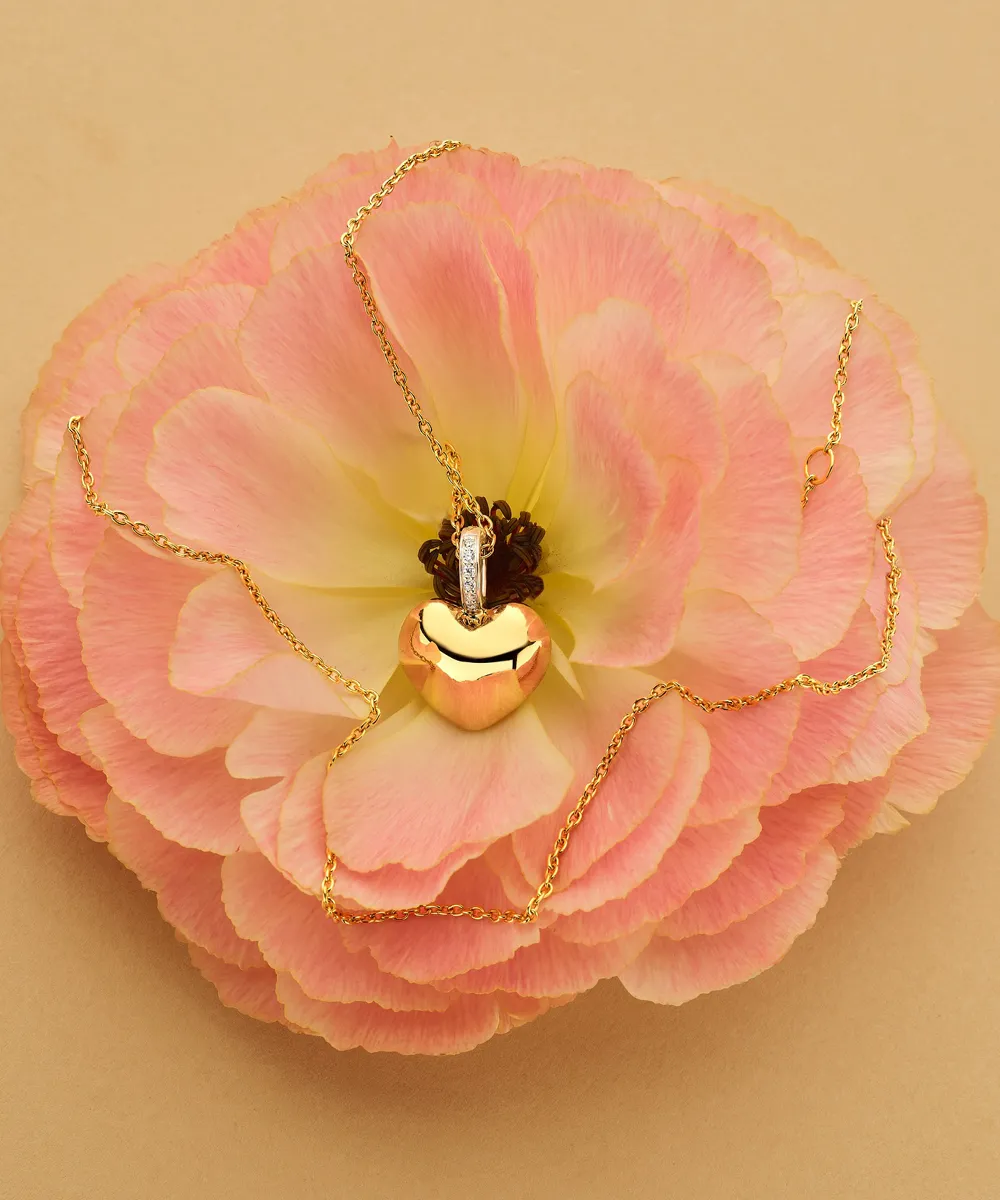 Gold heart pendant necklace on pink flower background.