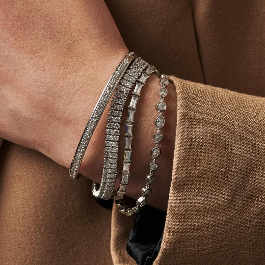 A hand wearing multiple diamond bracelets against a tan fabric background.