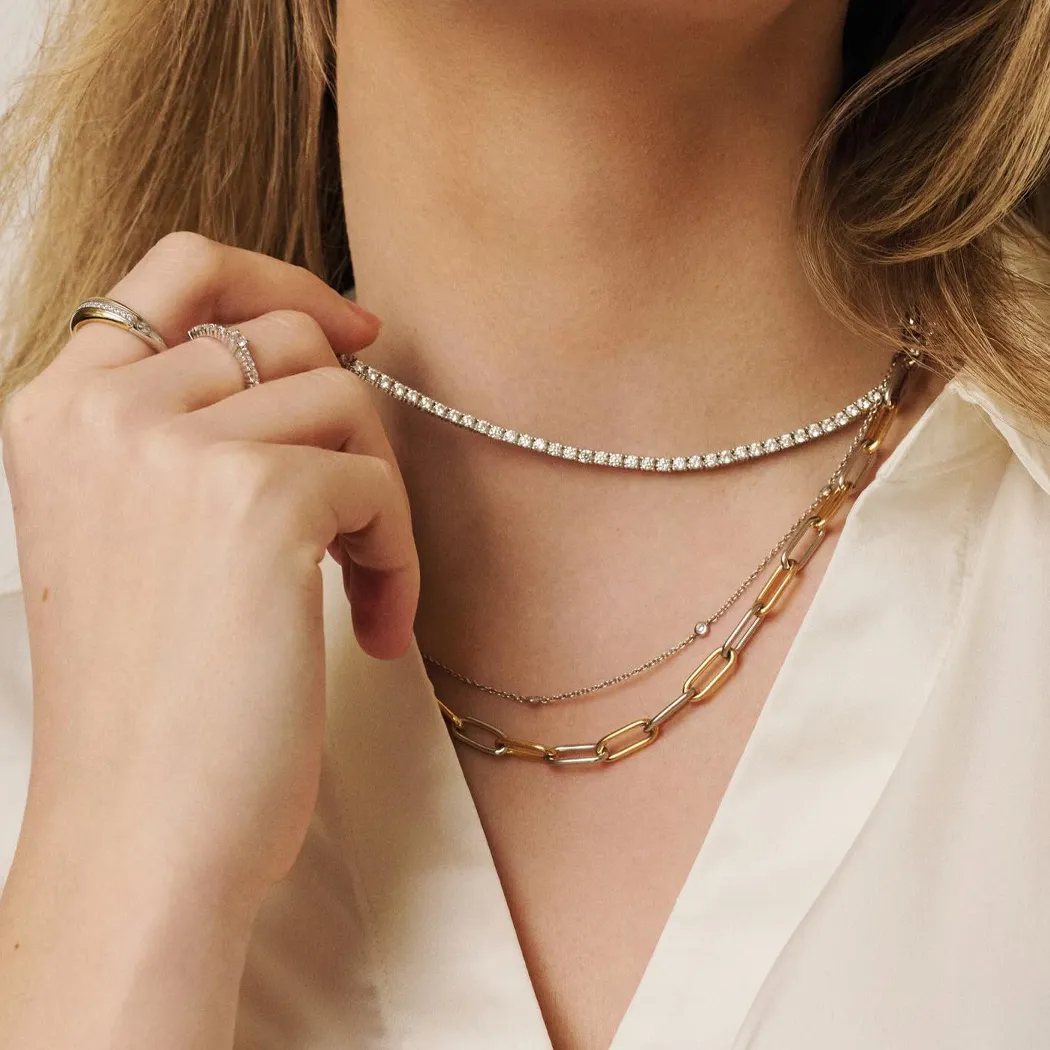 Close-up of a person wearing layered necklaces and rings, showcasing jewelry details.