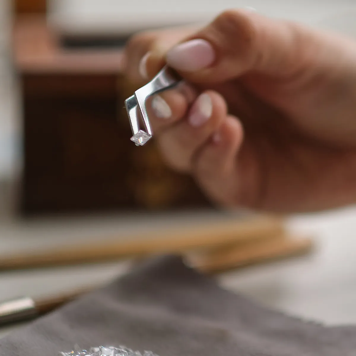 A hand holding a diamond with tweezers, showcasing jewelry craftsmanship.