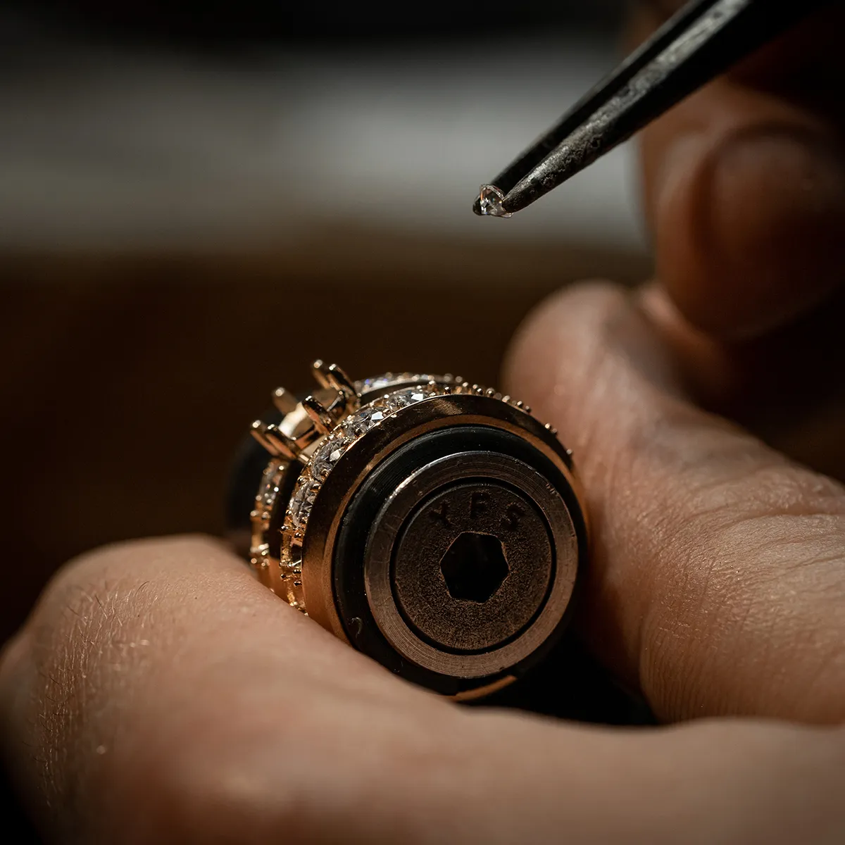 Close-up of a jeweler setting a diamond into a gold ring with tweezers.