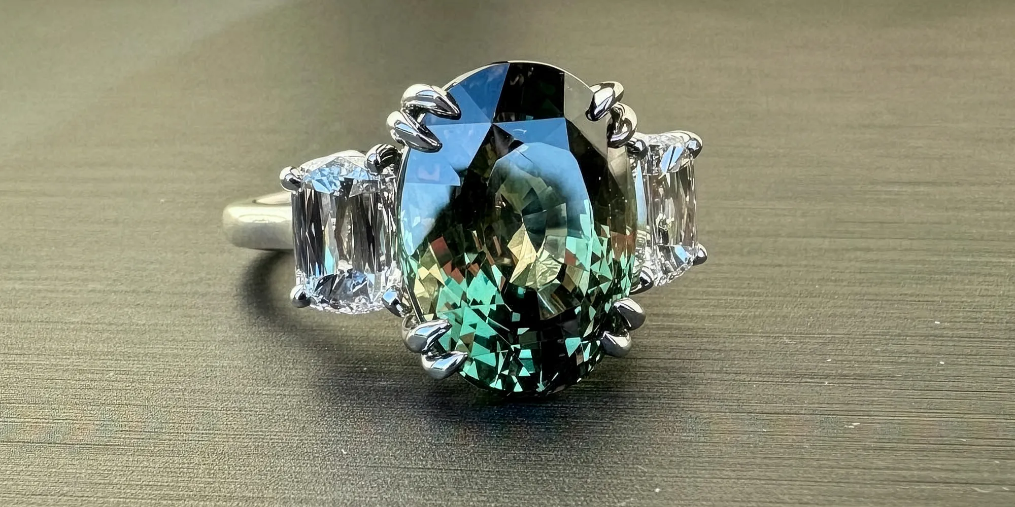 A ring with a large oval green gemstone and two side diamonds on a gray surface.