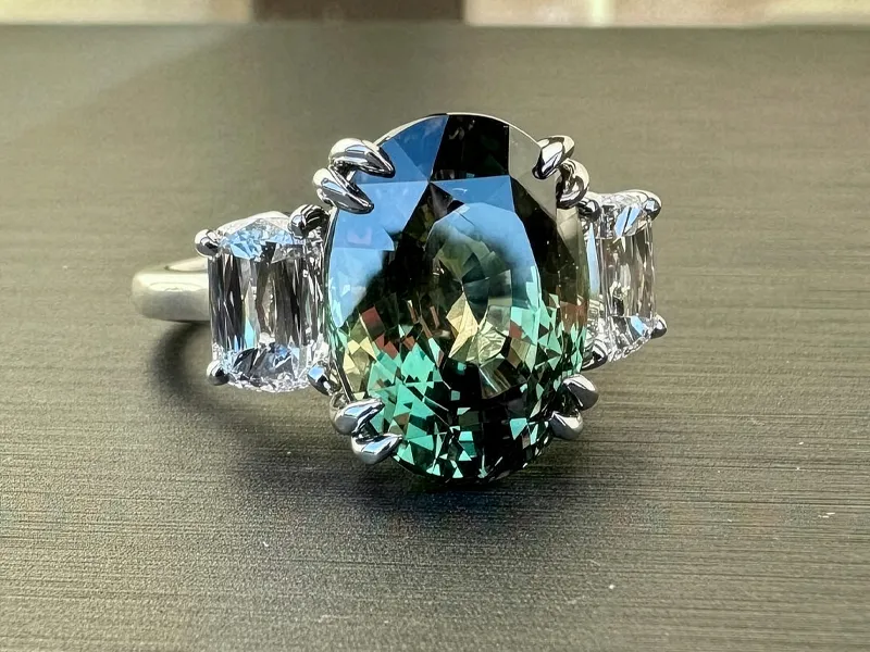 A ring with a large oval green gemstone and two side diamonds on a gray surface.