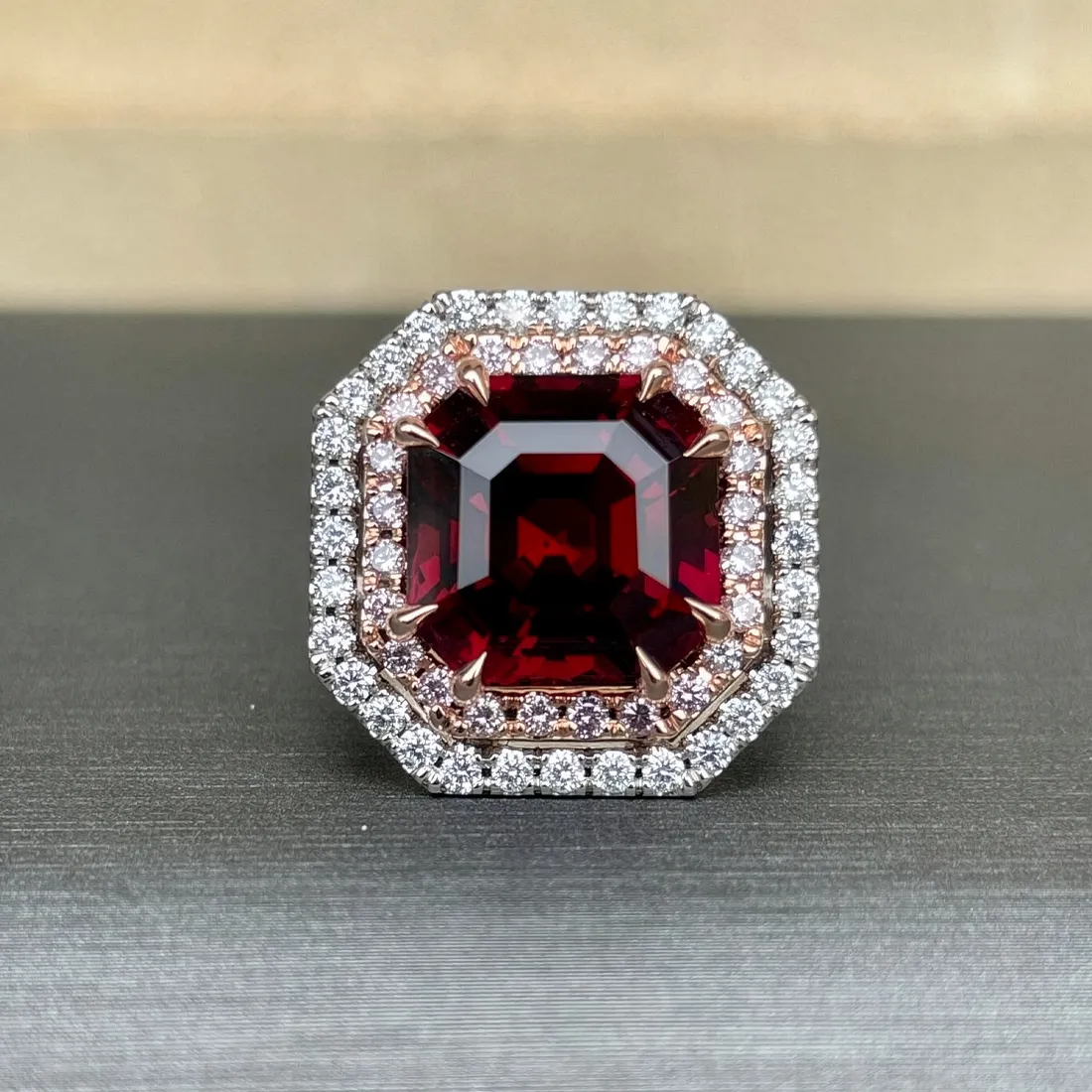 A large red gemstone ring with a diamond halo on a dark surface.