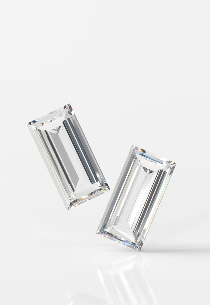 Two emerald-cut diamonds on a reflective surface.