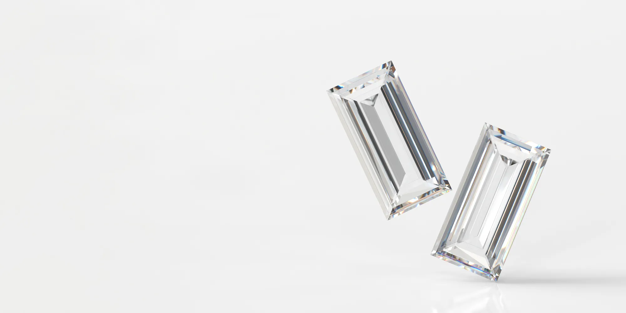 Two emerald-cut diamonds on a reflective surface.