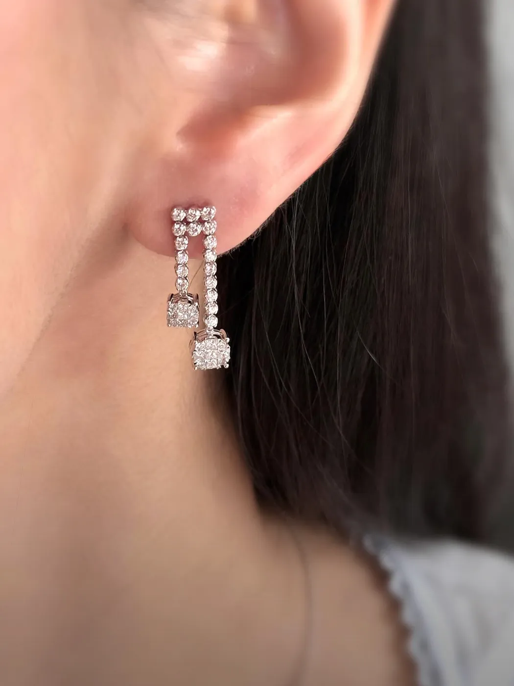 Close-up of a person's ear wearing elegant diamond earrings with a geometric design.