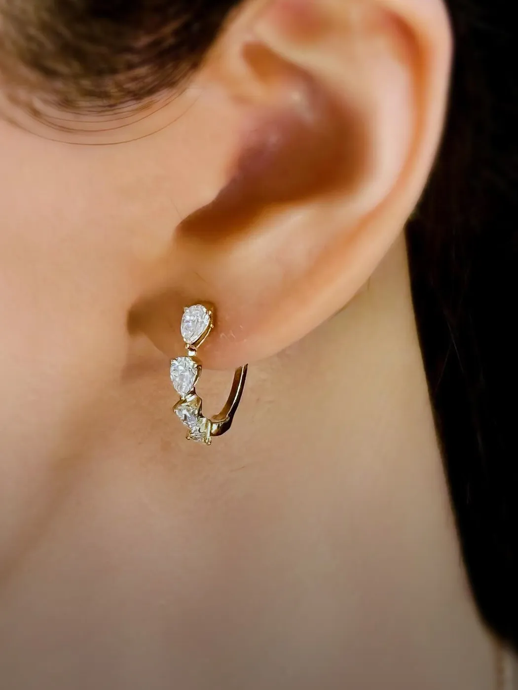 Close-up of an ear wearing a gold earring with three pear-shaped stones.
