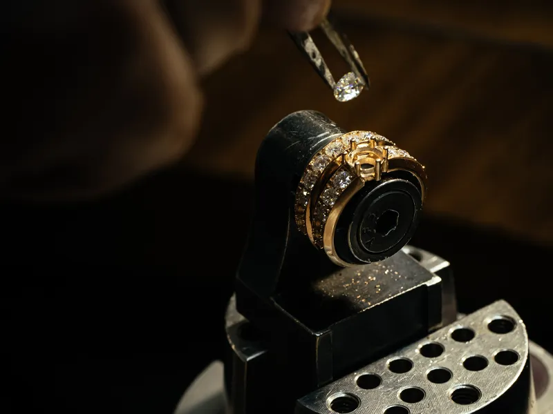 A jeweler uses tweezers to place a diamond on a gold ring.