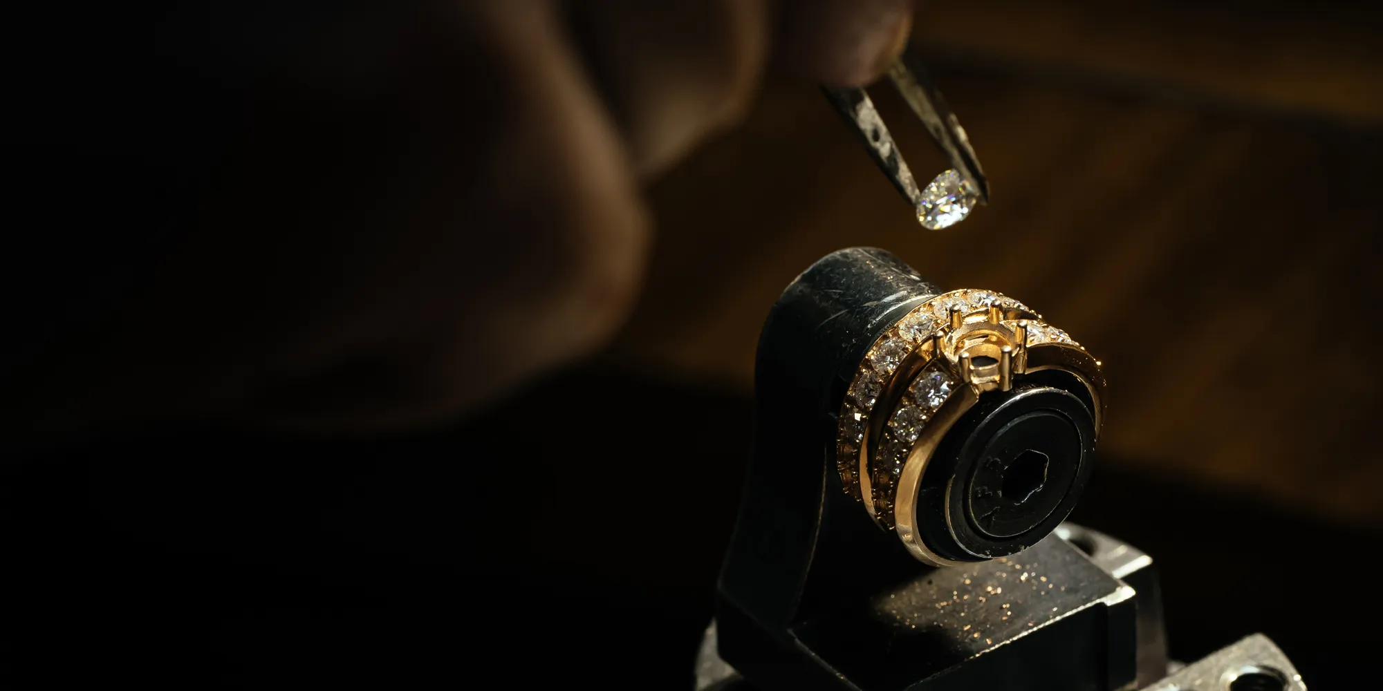 A jeweler uses tweezers to place a diamond on a gold ring.