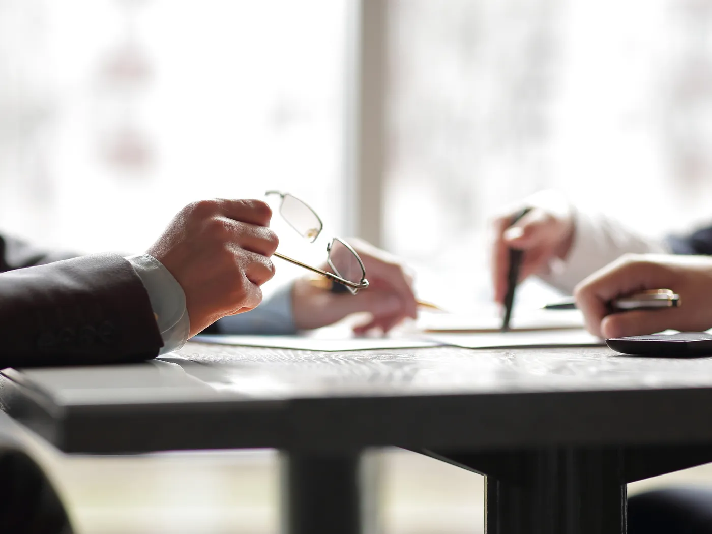 Business meeting with hands holding pens and glasses, discussing documents on a table.