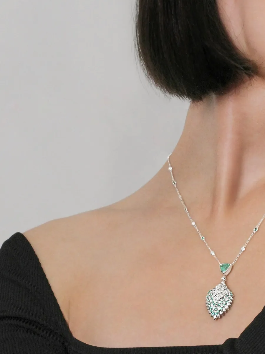 Woman wearing a silver necklace with a green gemstone pendant, off-shoulder black top.