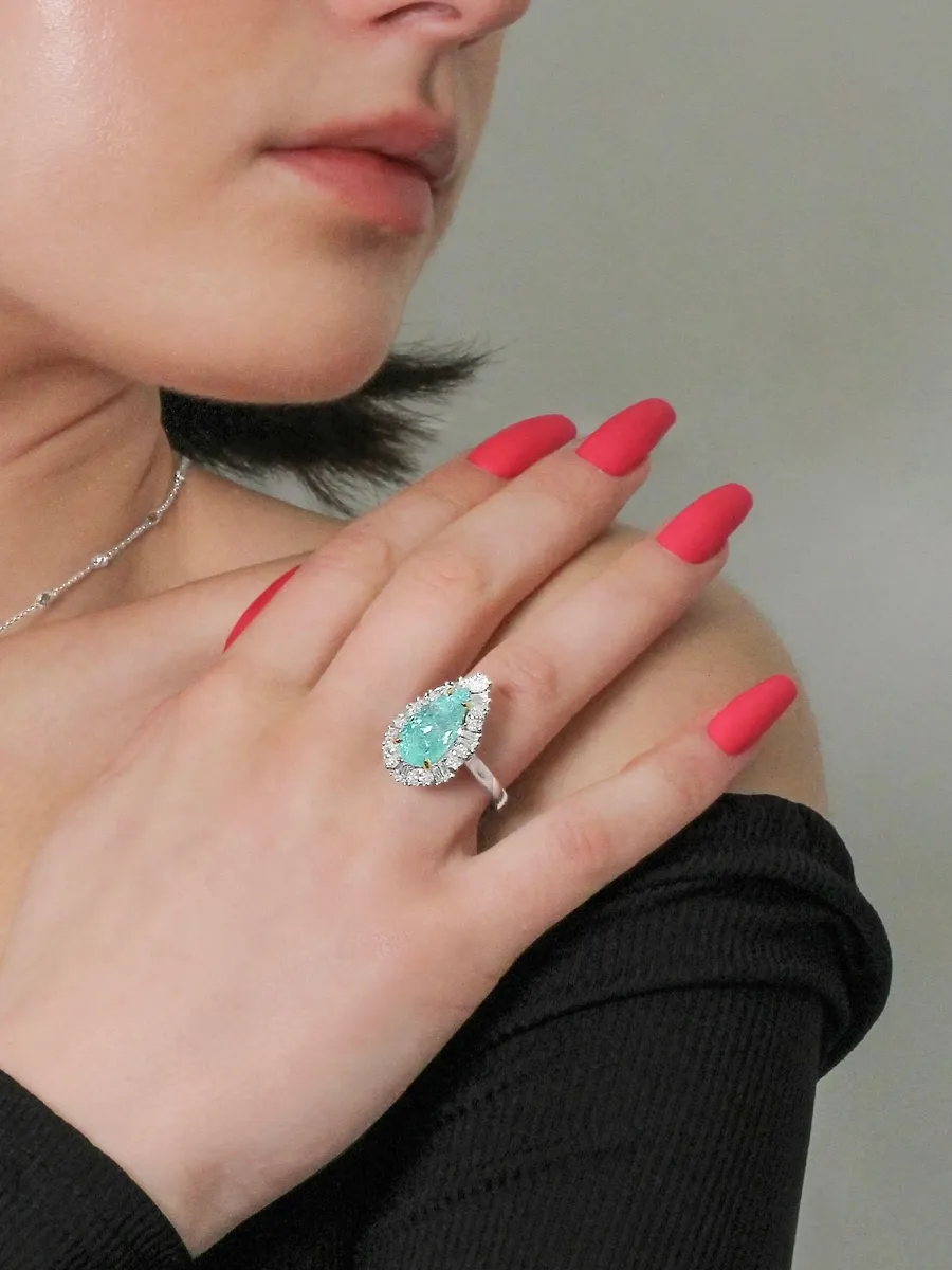 A woman with pink nails wearing a large pear-shaped gemstone ring on her hand.