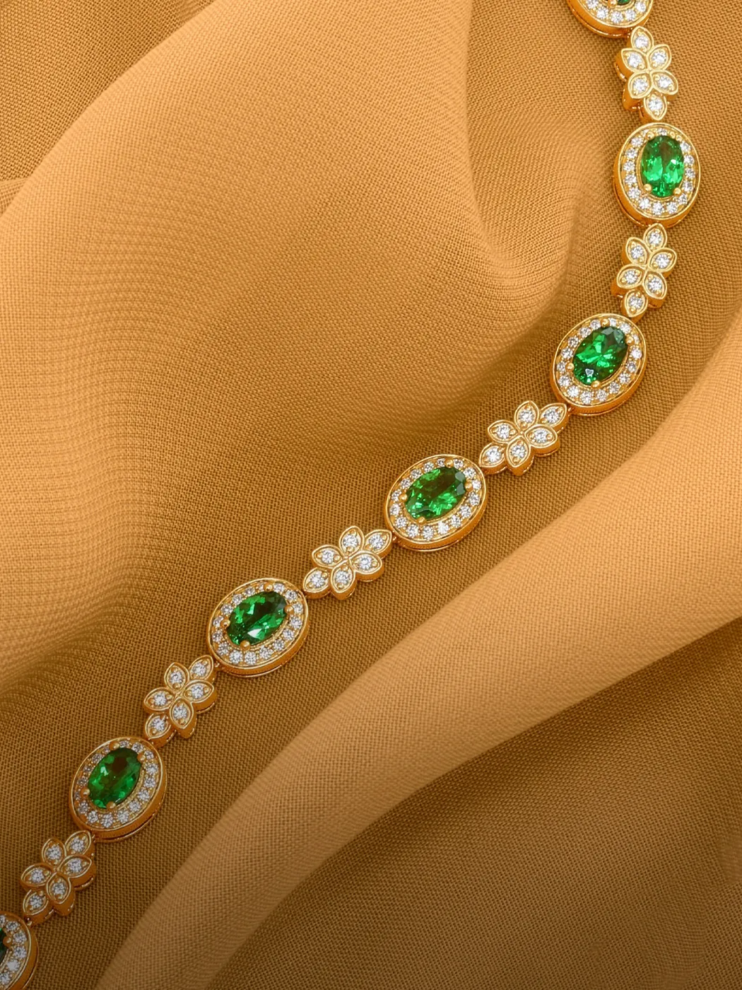 Elegant gold bracelet with green gemstones and diamonds on a textured fabric background.