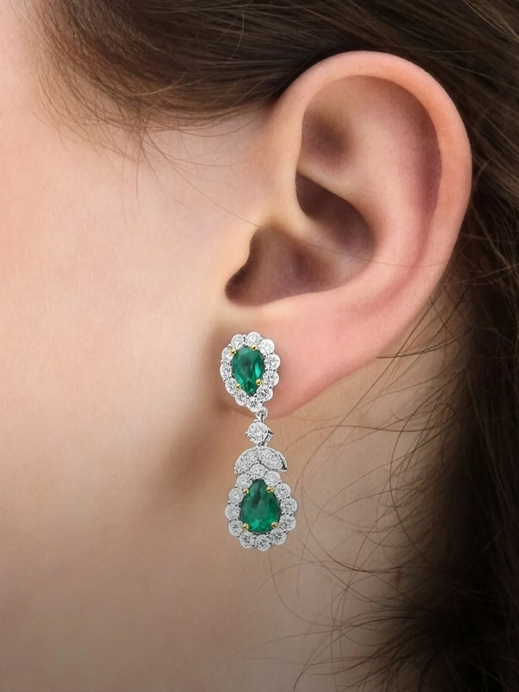 Emerald and diamond earrings worn on an ear.