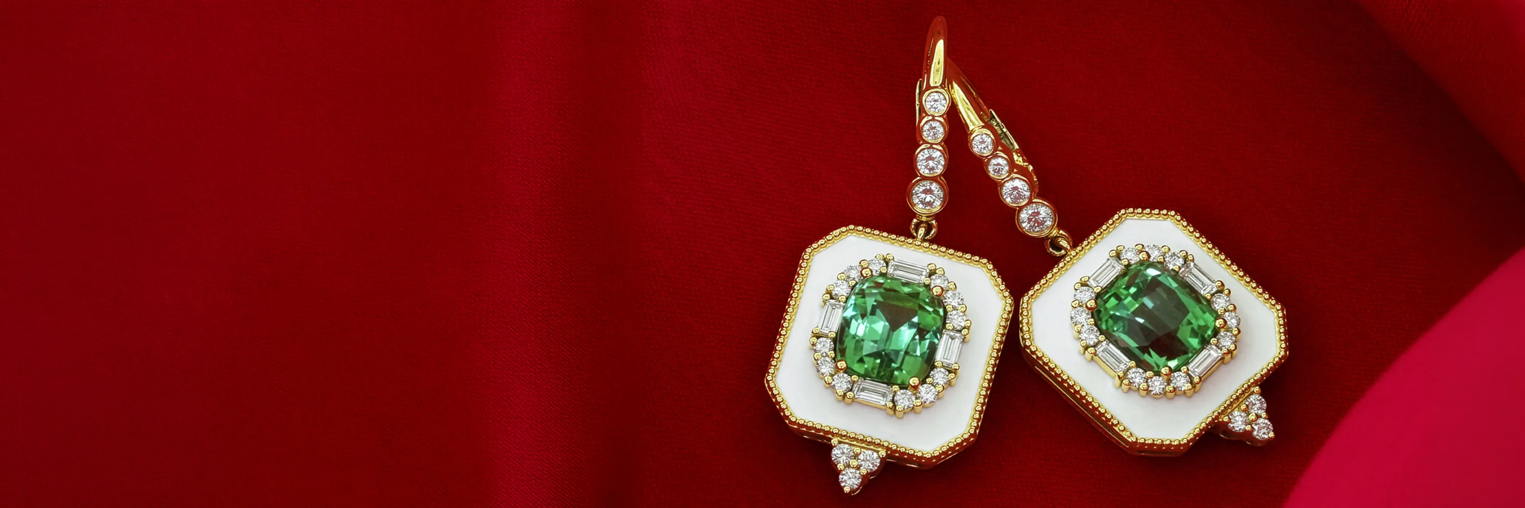 Elegant green gemstone earrings with diamonds on a red fabric background.