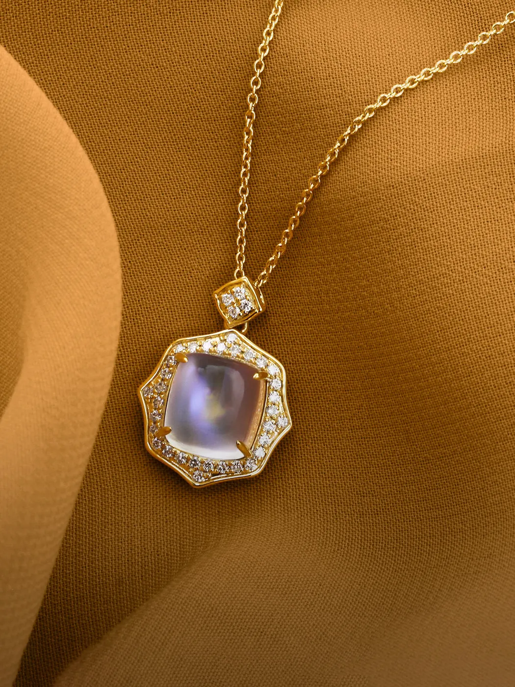 Gold necklace with a square gemstone pendant and diamond accents on a brown fabric background.