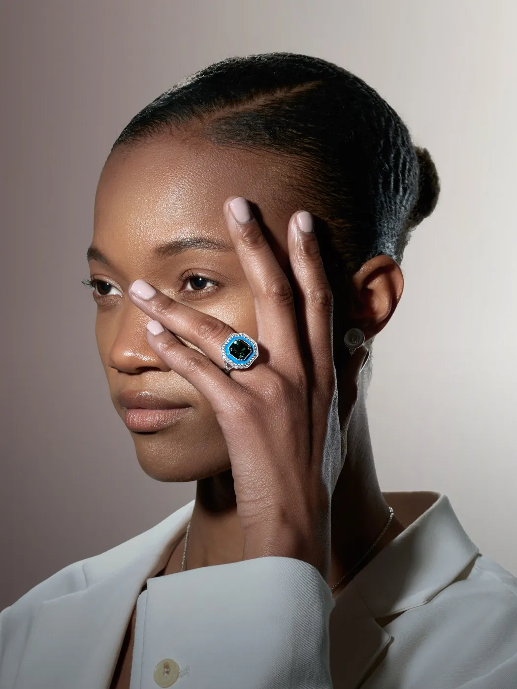 A person wearing a blue gemstone ring covers part of their face with their hand.