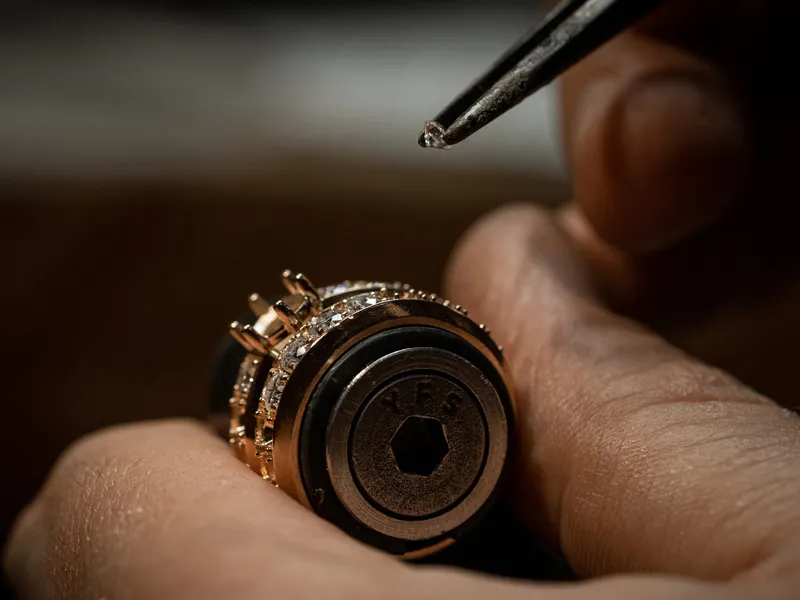 Close-up of hands setting a small diamond into a gold jewelry piece with tweezers.