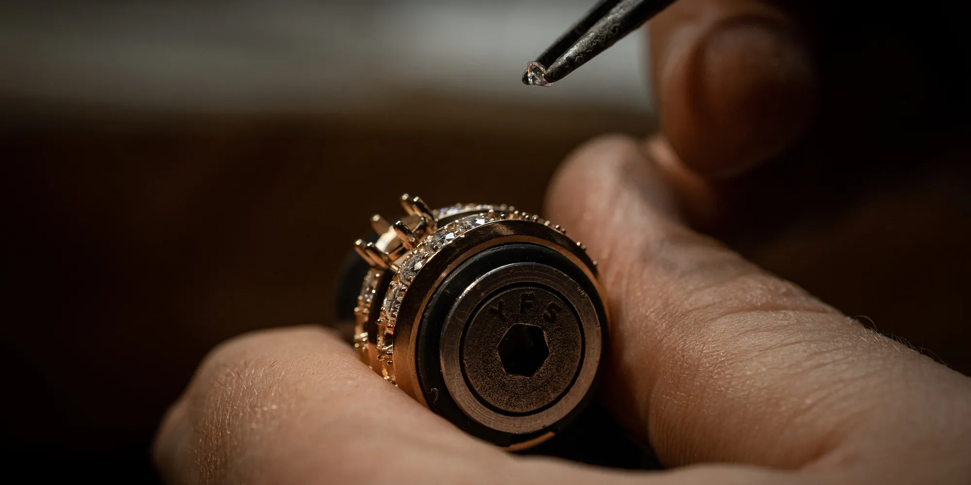 Close-up of hands setting a small diamond into a gold jewelry piece with tweezers.