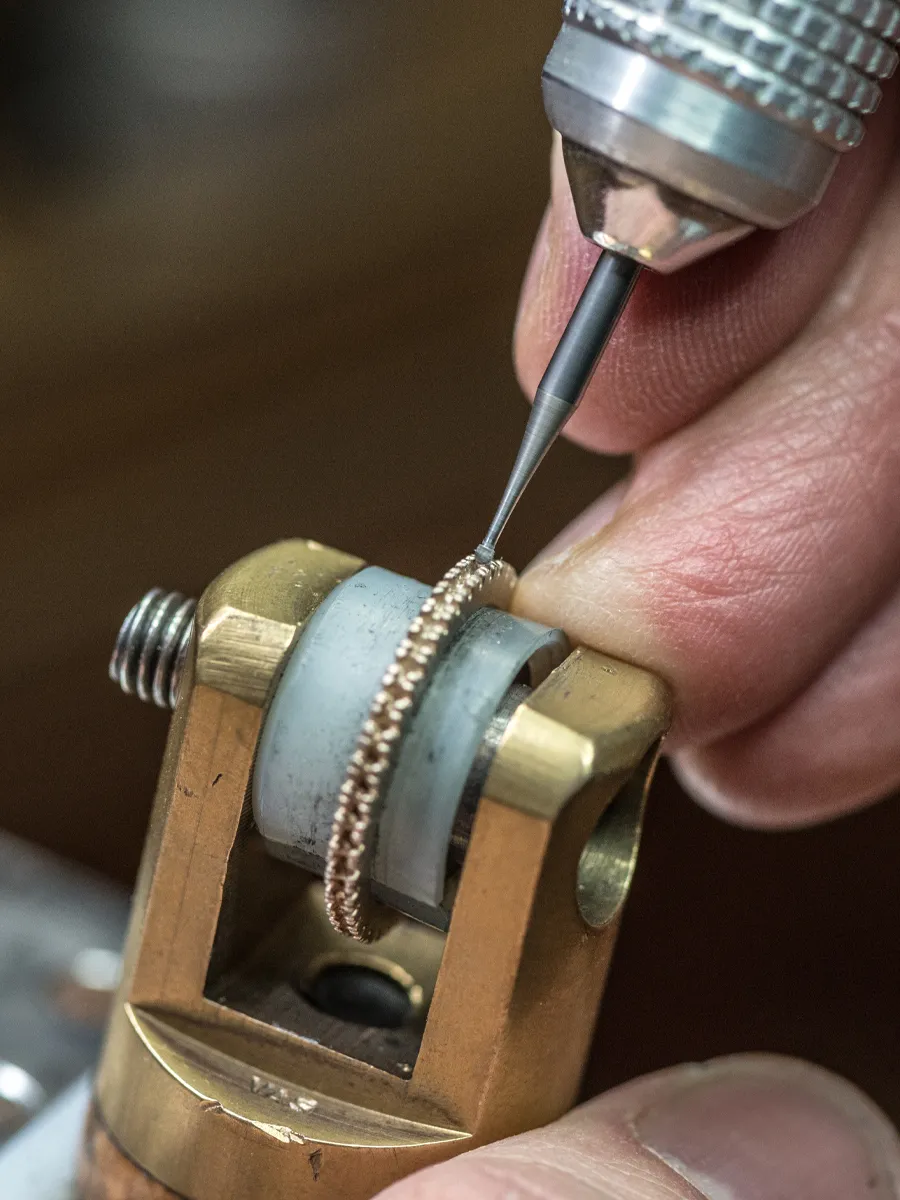 A jeweler uses a precision tool to engrave a detailed pattern on a ring.