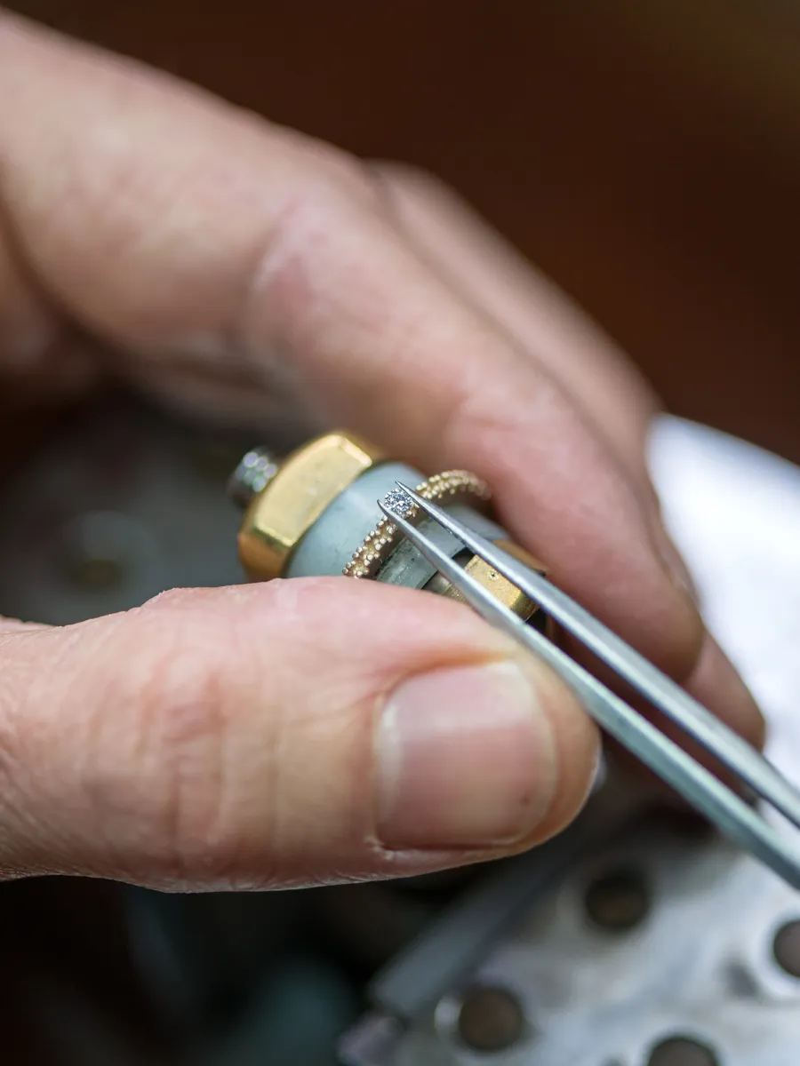 Close-up of a hand using tweezers to hold a small jewelry component.