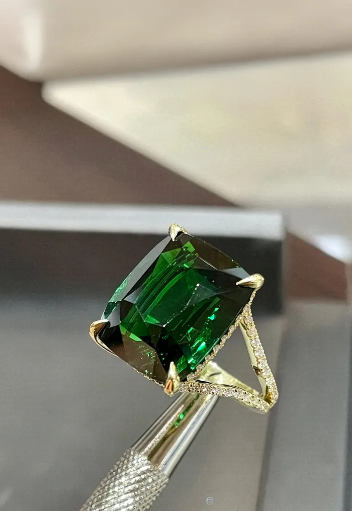 A green gemstone ring held by tweezers, showcasing its brilliance.