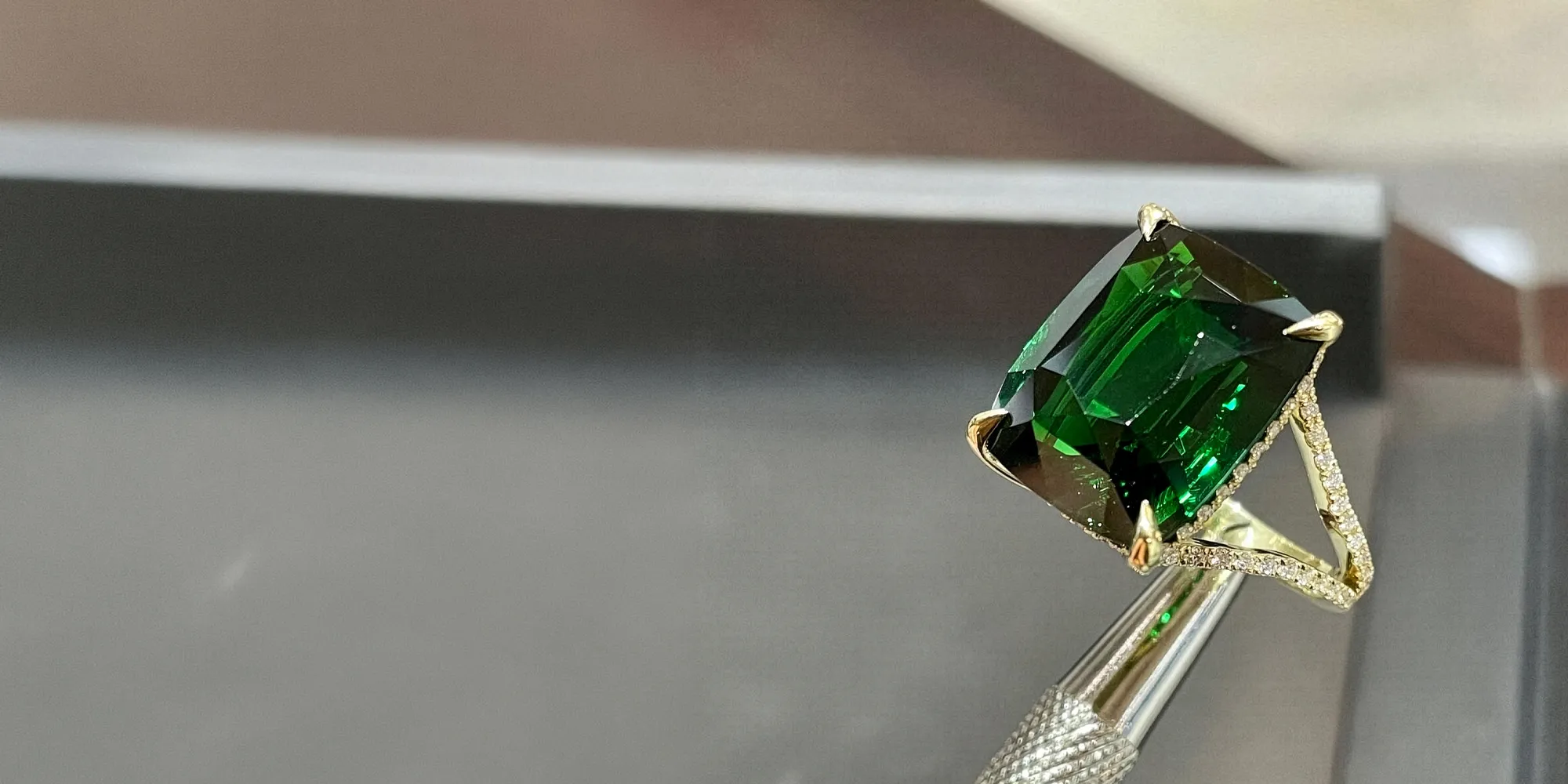 A green gemstone ring held by tweezers, showcasing its brilliance.