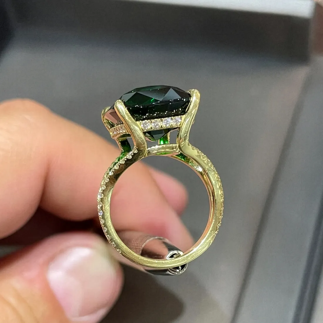 A hand holding a gold ring with a large dark gemstone and diamond accents.