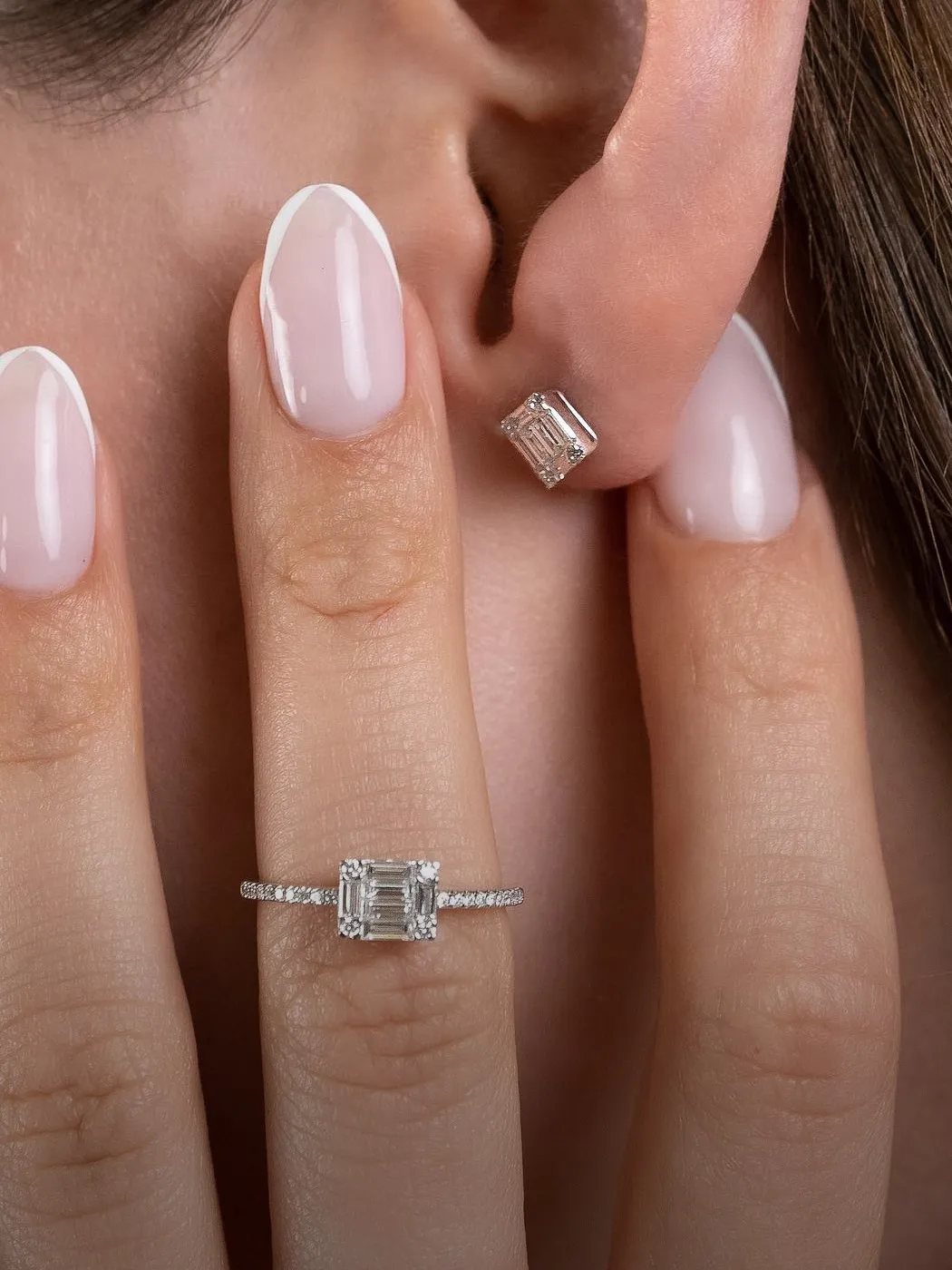 A hand with a diamond ring and matching earring, showcasing fine jewelry.