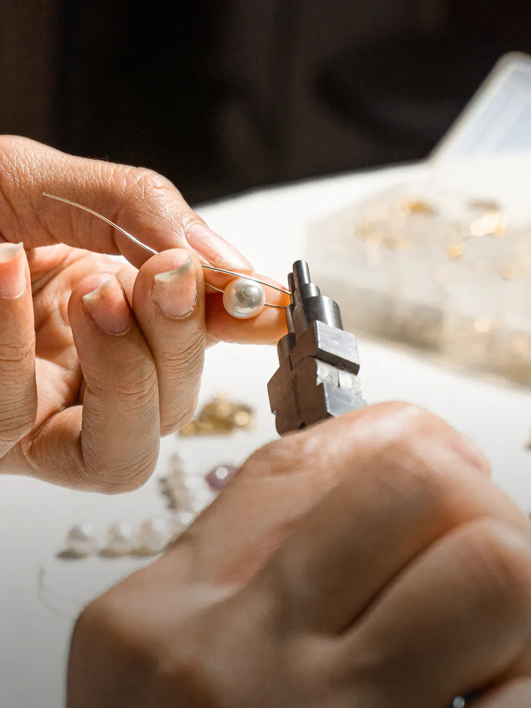 Hands using pliers to restring a pearl on a wire at a jewelry workshop.
