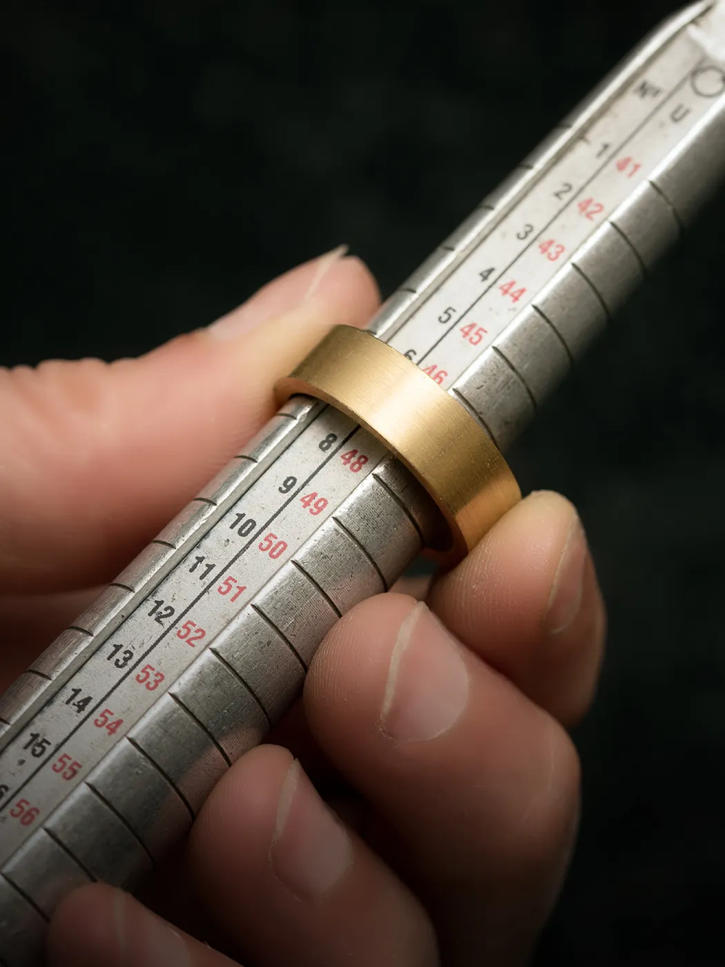 A gold ring on a ring sizer, held by a hand, indicating ring resizing service.