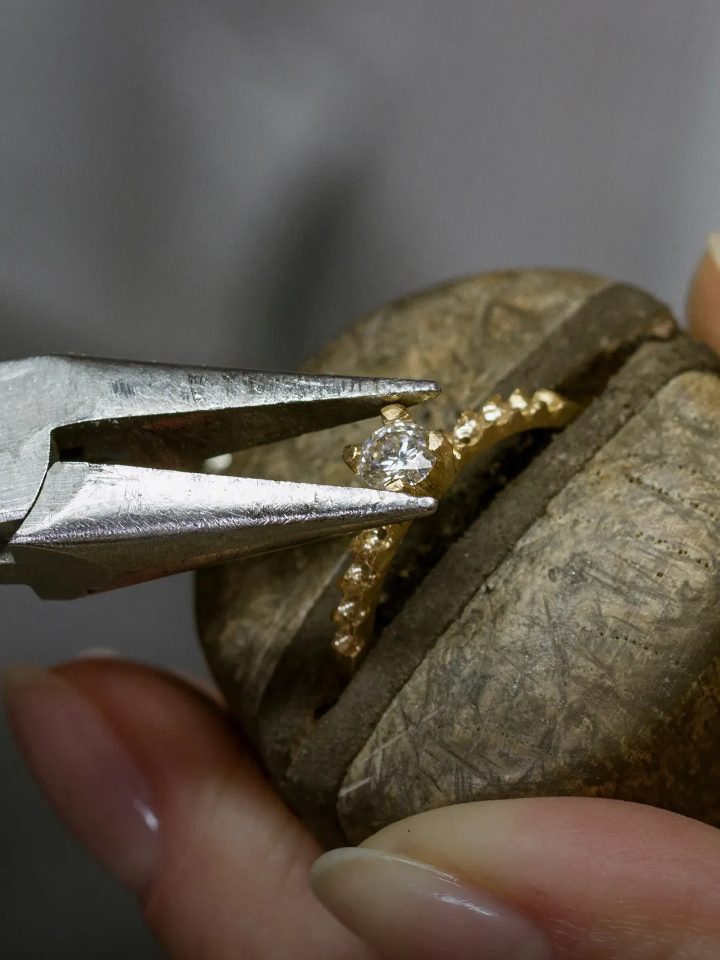 Jeweler using pliers to repair a diamond ring prong on a wooden holder.