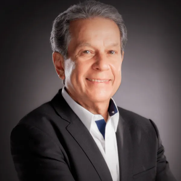 Man in a suit smiling against a dark background.