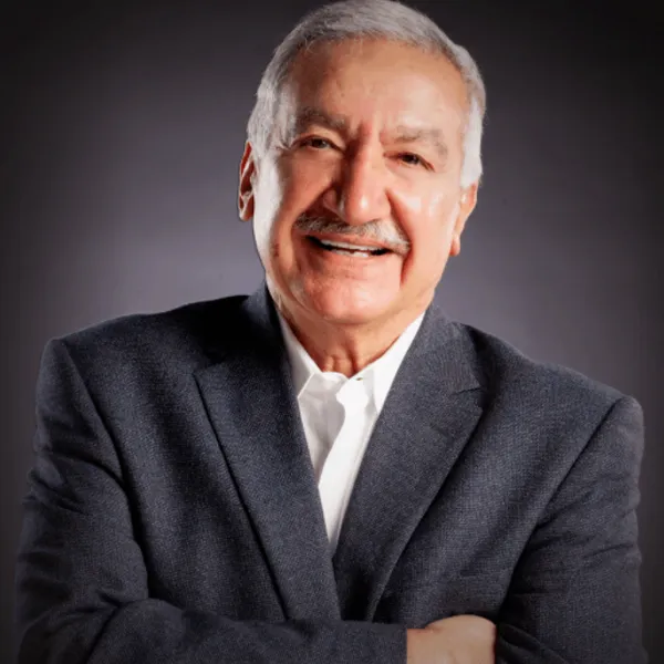 Smiling man in a suit with arms crossed against a dark background.