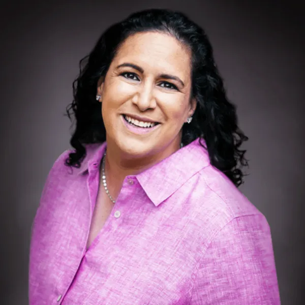 Smiling person in a pink shirt with a dark background.