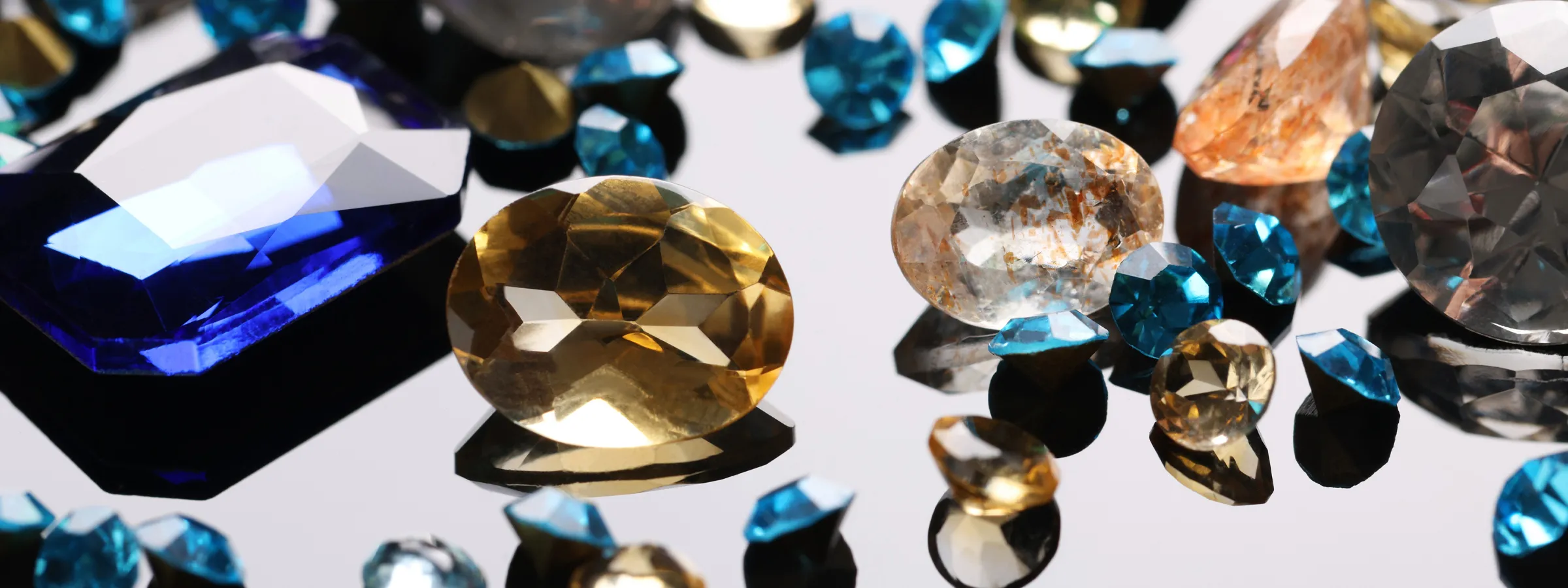 Colorful assortment of gemstones including blue, yellow, and clear stones, reflecting light on a shiny surface.