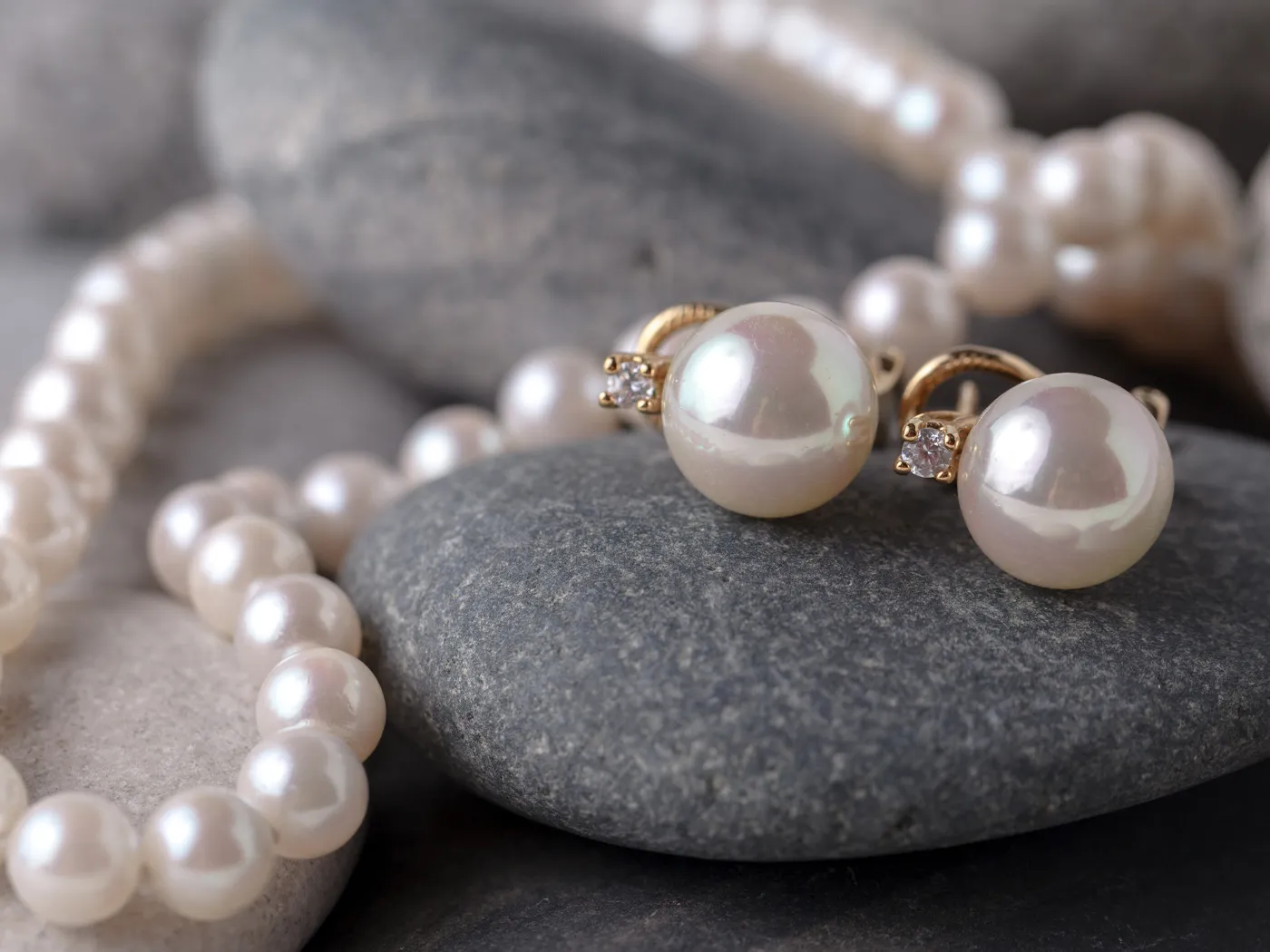 Elegant pearl earrings and necklace resting on smooth stones, showcasing fine jewelry from Dominion Jewelers in Falls Church.