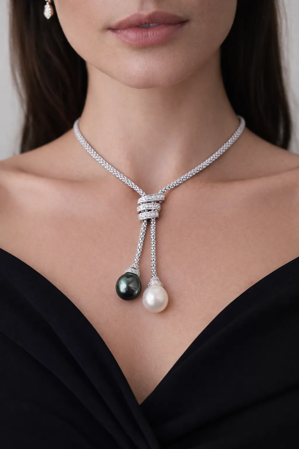Woman wearing a pearl pendant necklace and a gemstone ring on a white shirt.