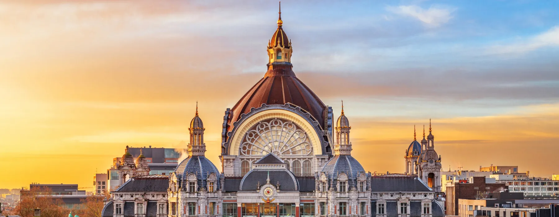 Ornate historic building with domed roof at sunset, cityscape in background.