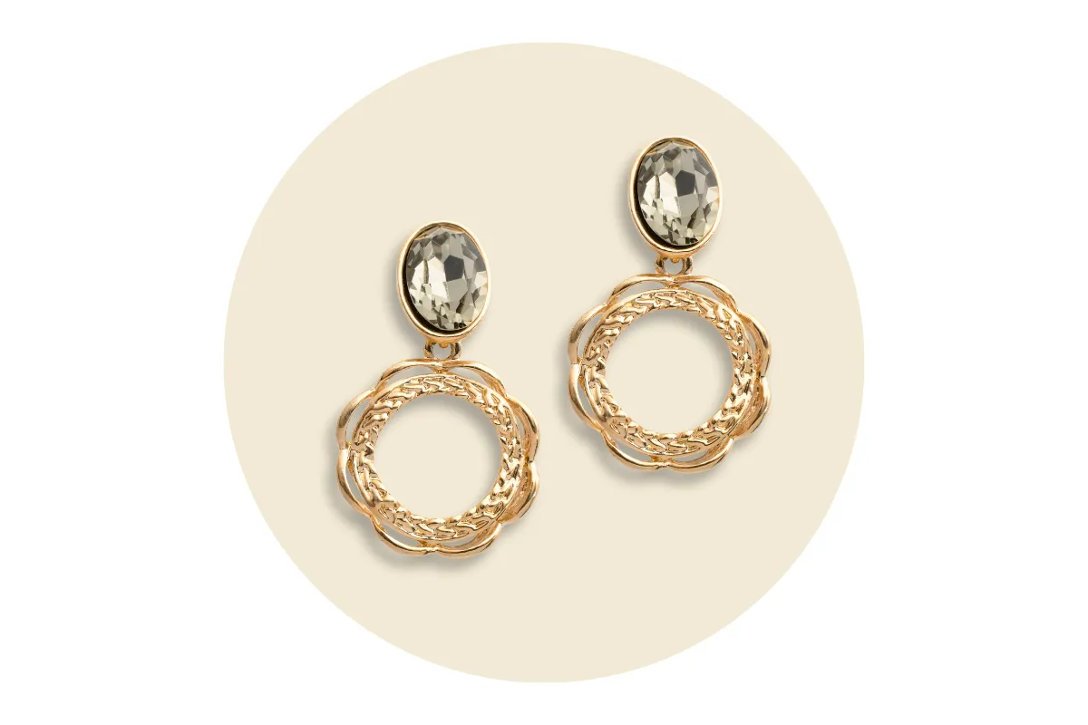 Estate gold earrings with oval stones and intricate circular design on a beige background.
