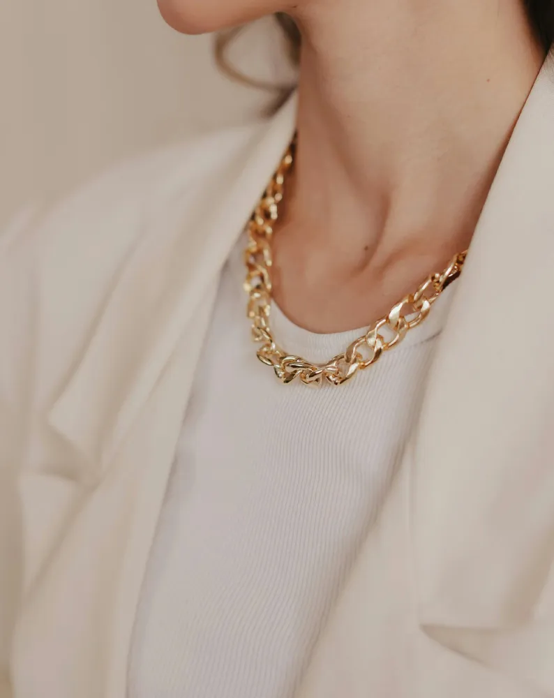 Close-up of a woman wearing a gold chain necklace with a white top and blazer.
